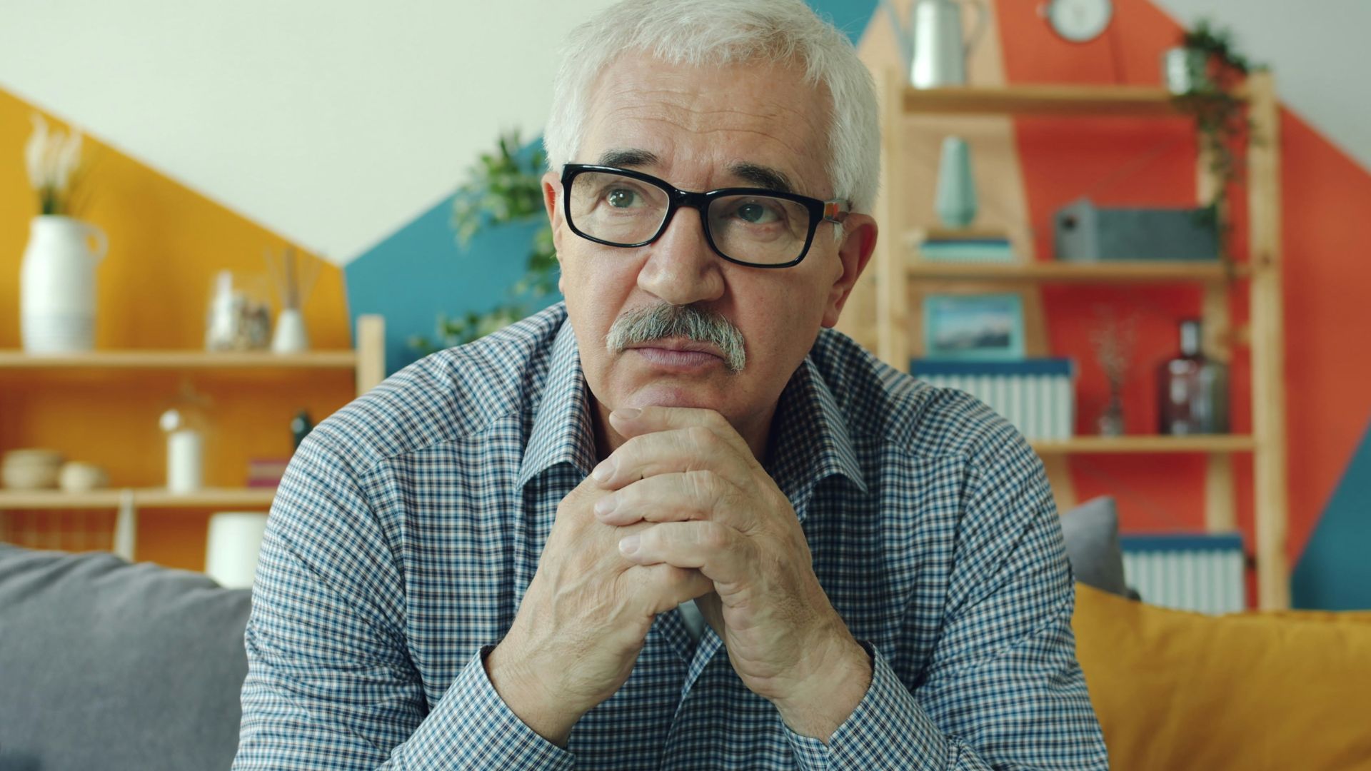 Elderly man with glasses resting chin on hands.