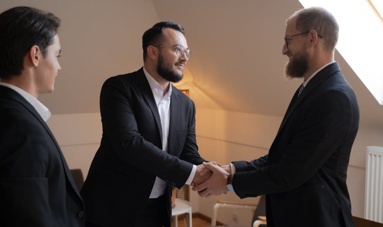 Bearded Men in Black Suit Doing Handshake while Looking at Each Other