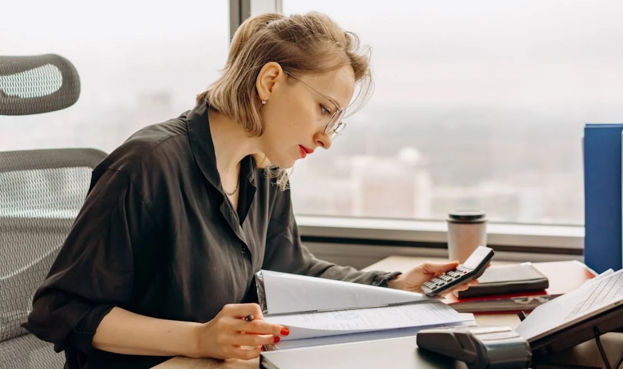 Woman in Polo Long Sleeves Computing Using a Calculator