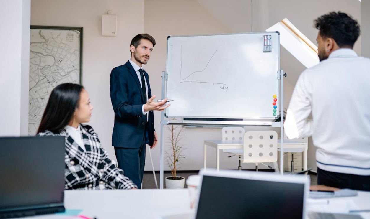 A Man in Blue Suit Jacket Standing Beside the Whiteboard
