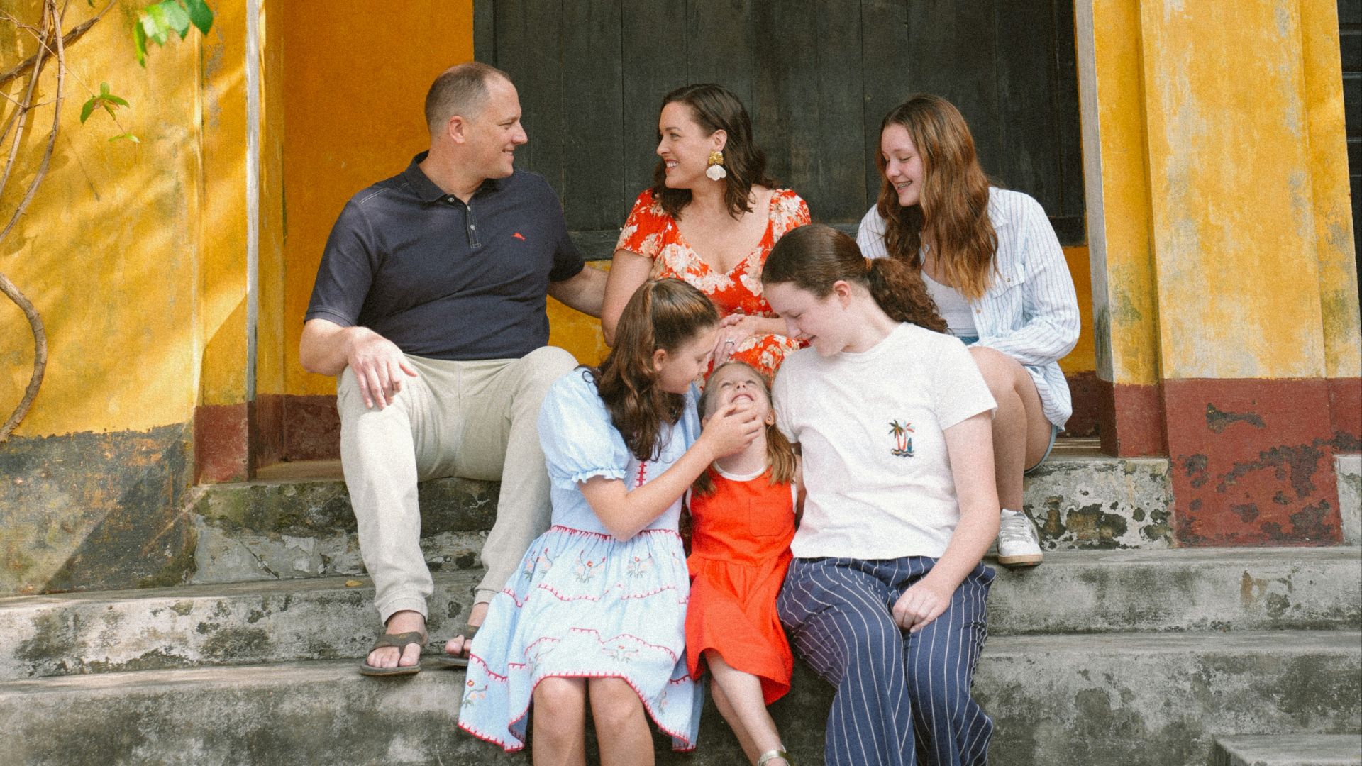 Family posing on steps of a yellow building