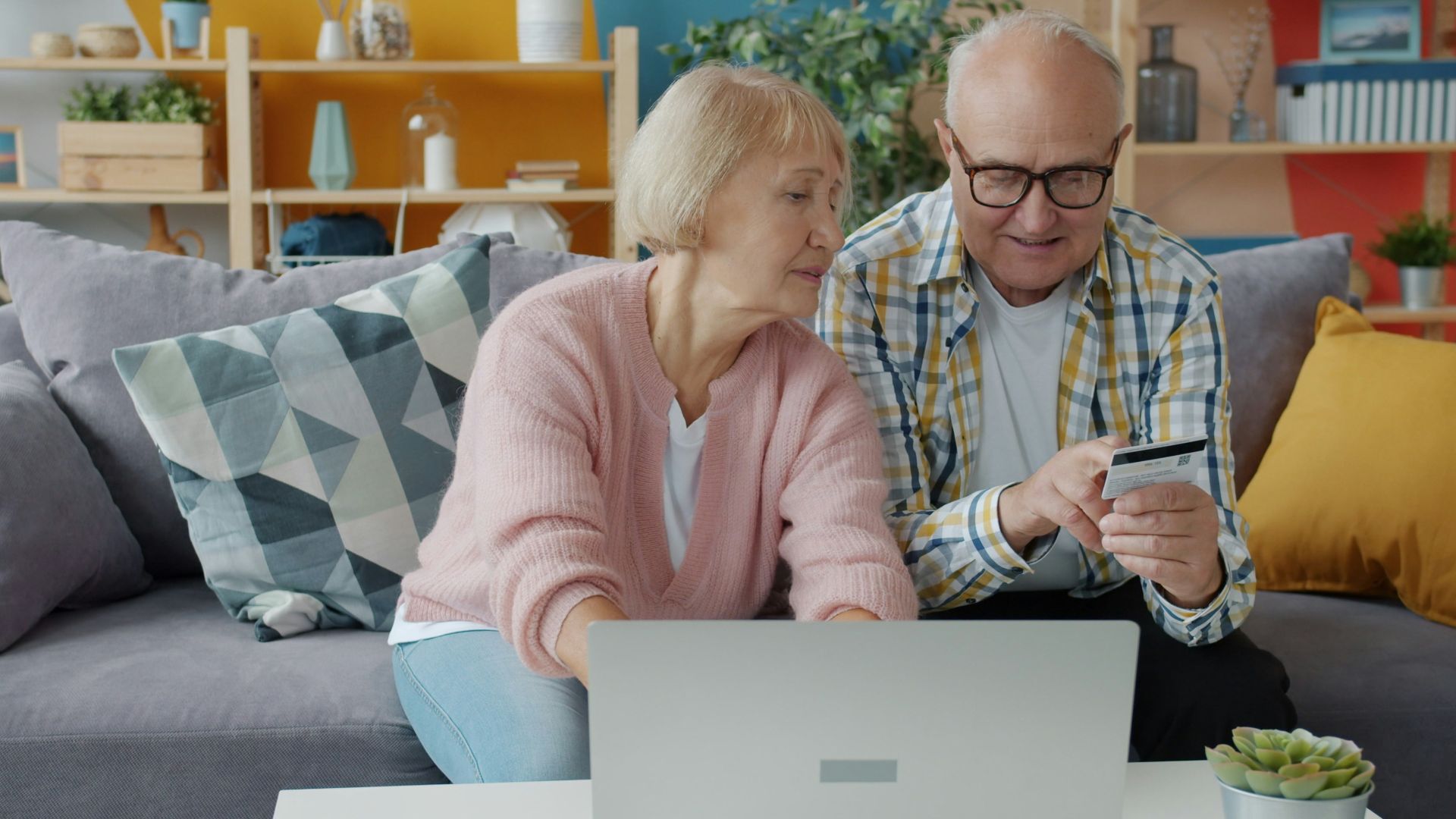 Elderly couple shopping online with credit card and laptop.