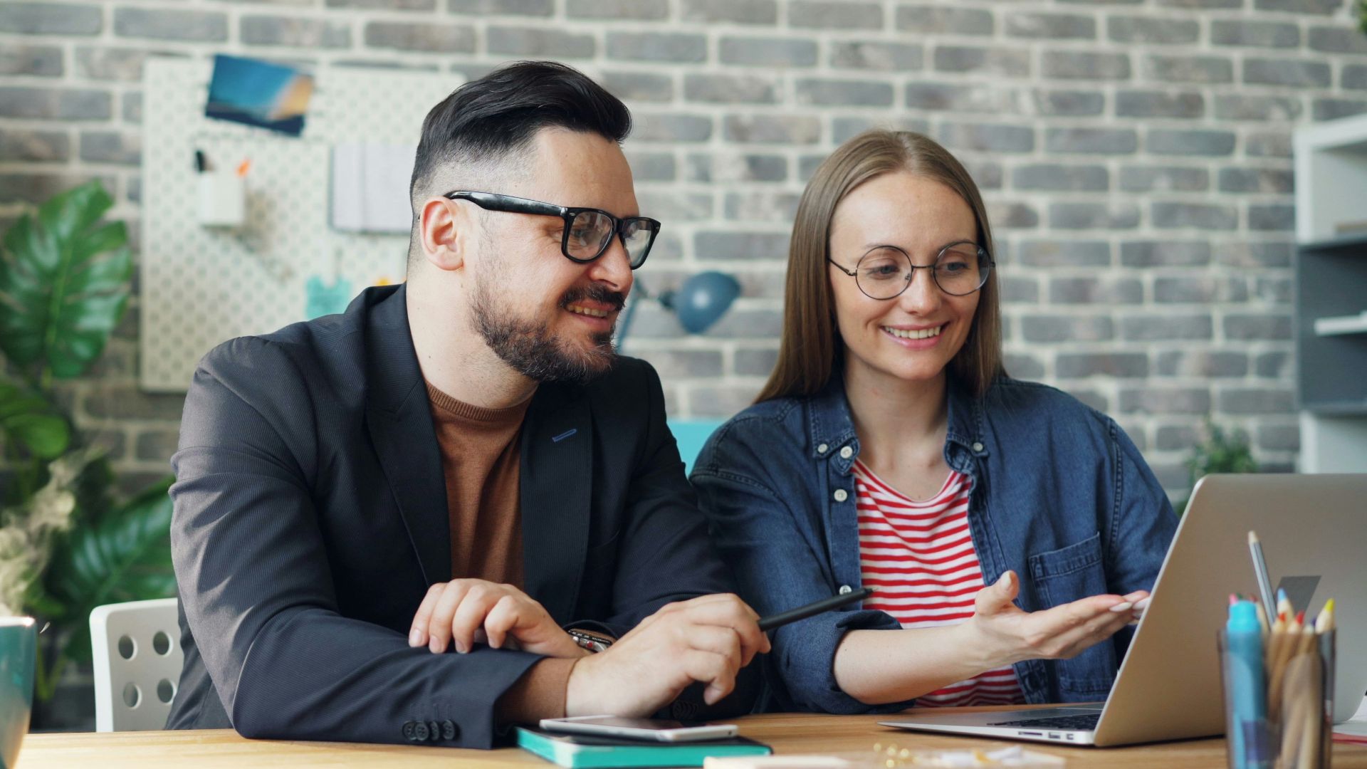 a man and a woman sitting at a table looking at a laptop