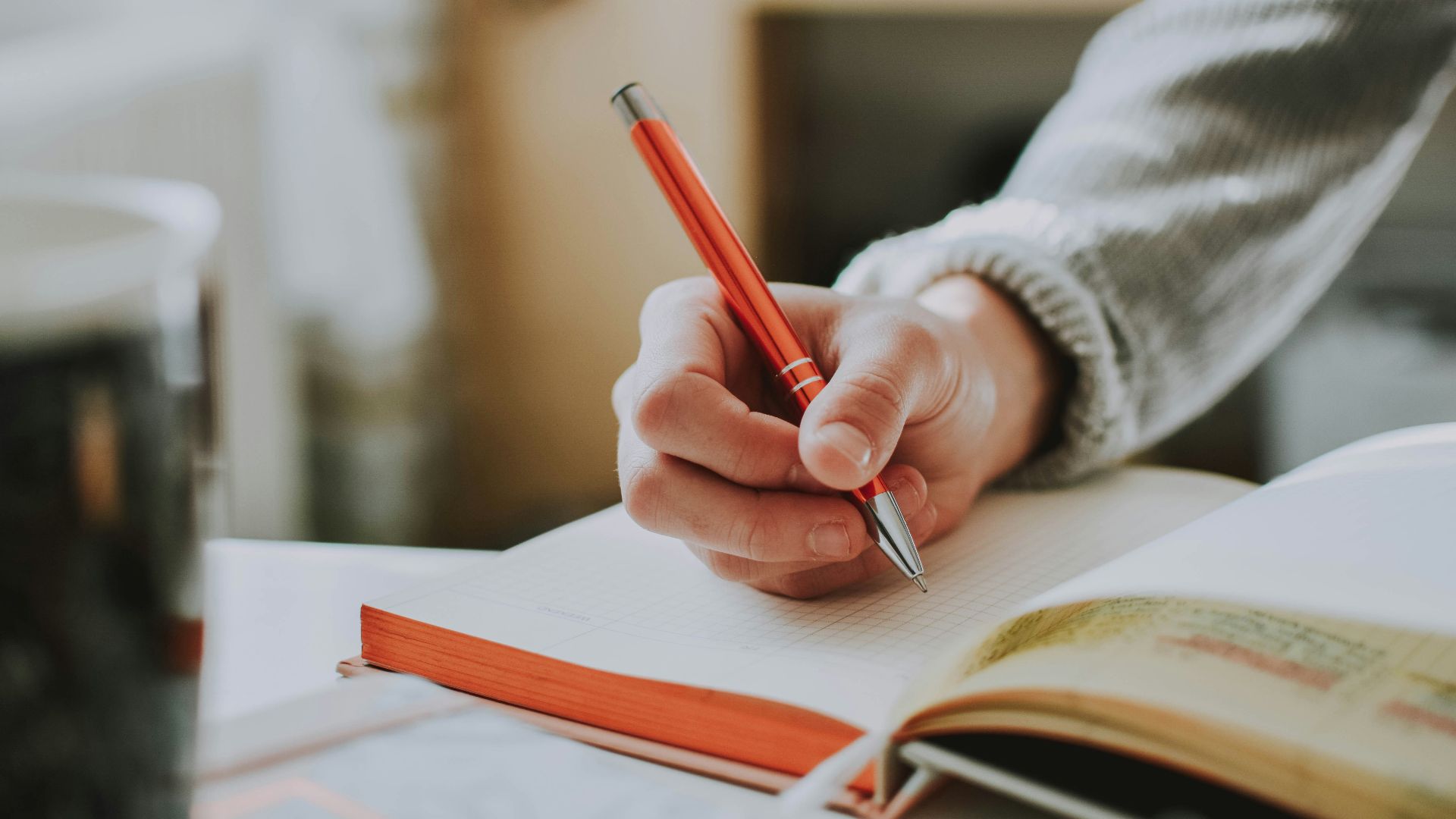 person holding on red pen while writing on book