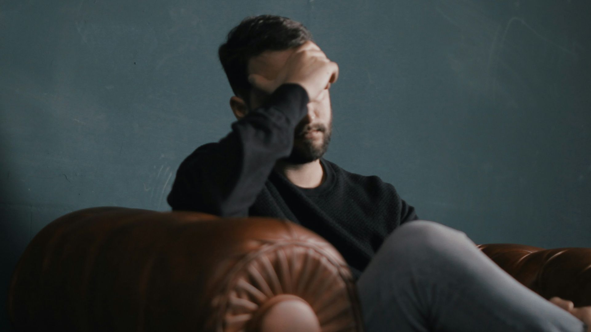 a man holds his head while sitting on a sofa