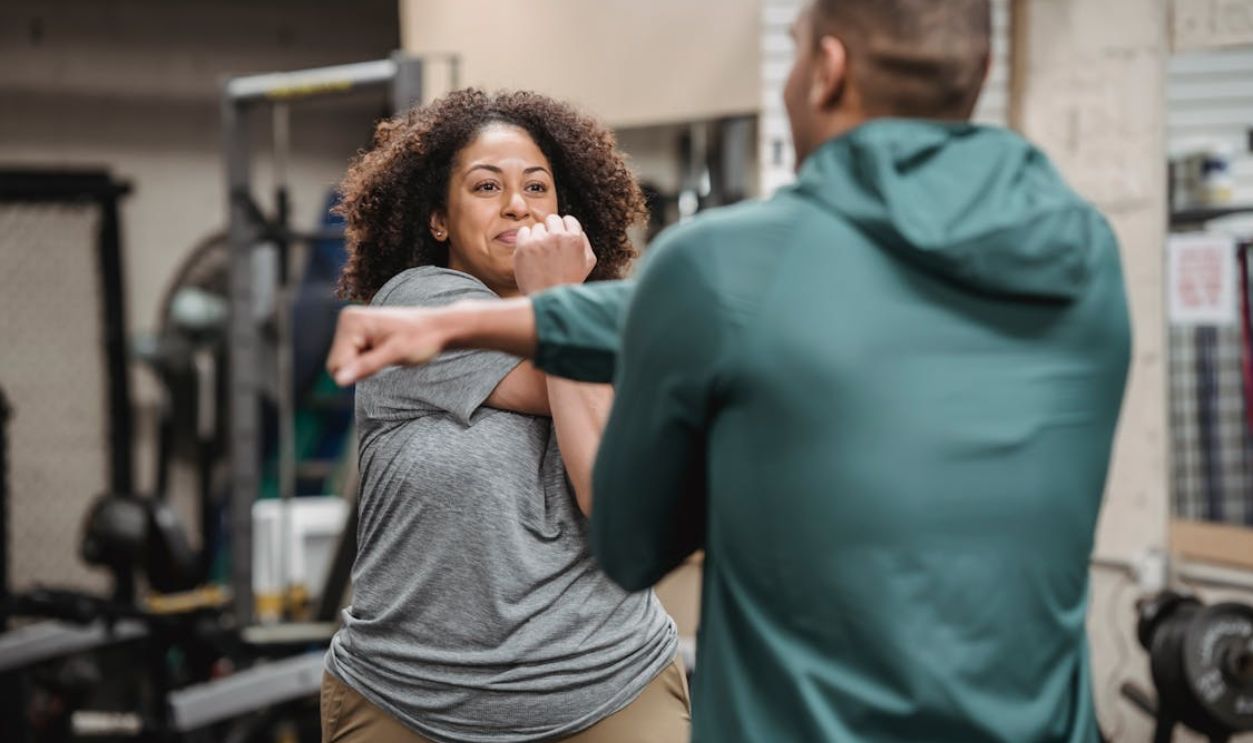 Trainer warming up with black woman in gym