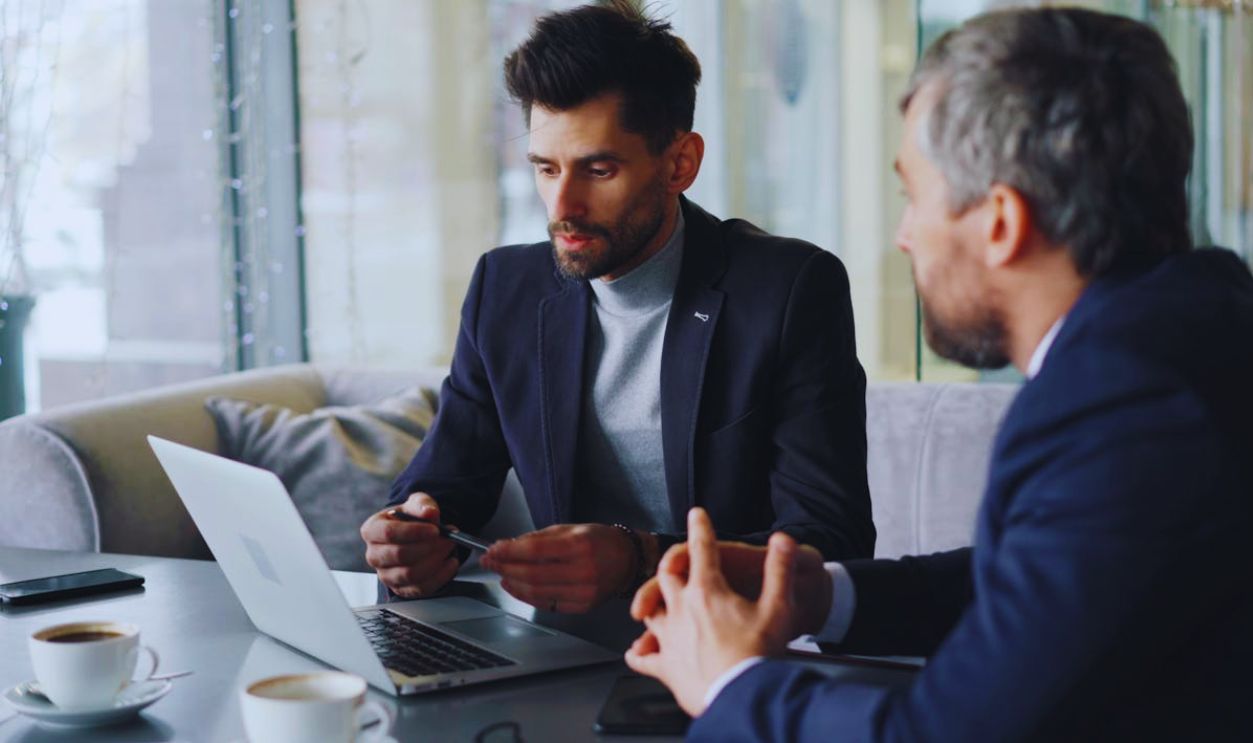 Two men in business attire sitting at a table with laptops