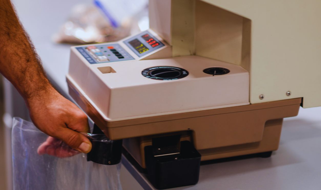 Man filling a plastic bag with metal coins after counting them on a electronic machine that is used for counting and sorting