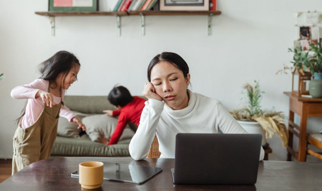 Tired ethnic working mother at home with playing kids