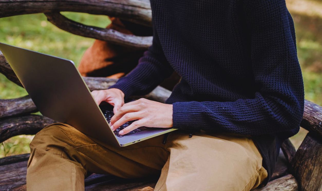 Crop unrecognizable man typing on laptop in park