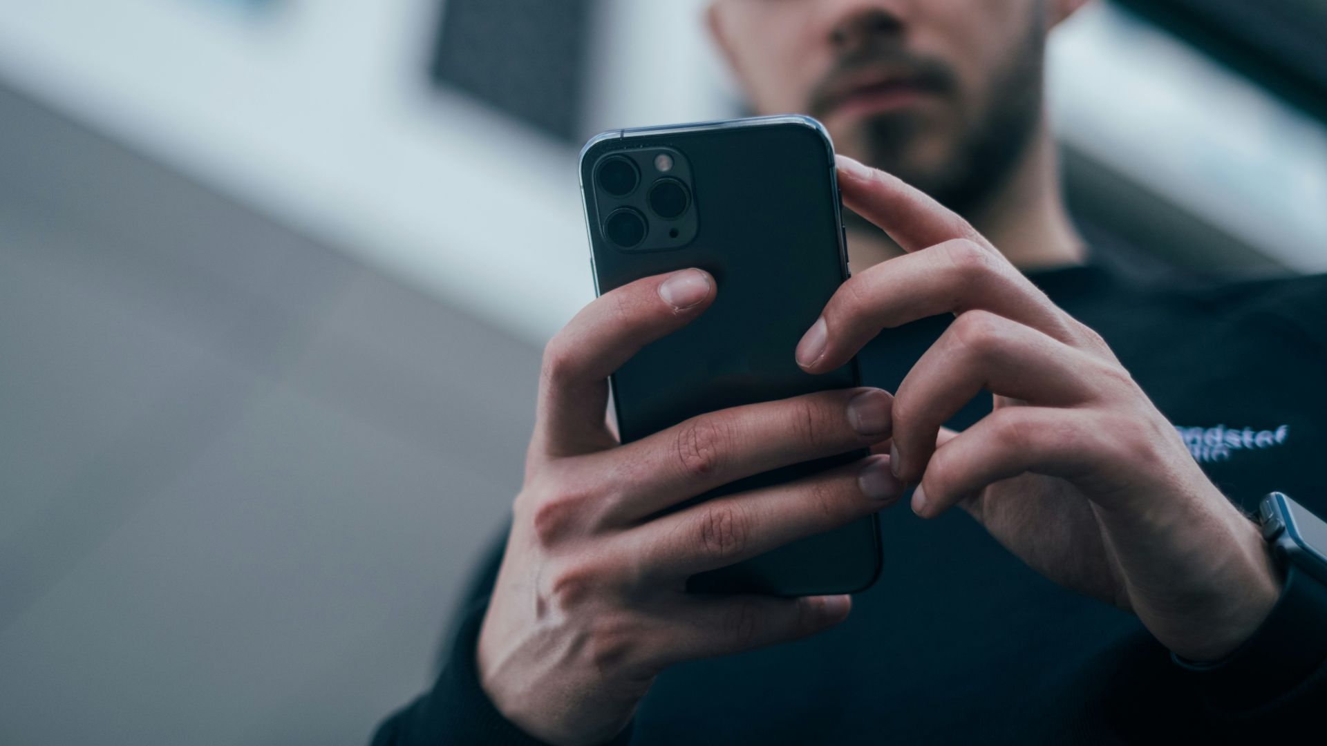 man wearing black sweater using smartphone
