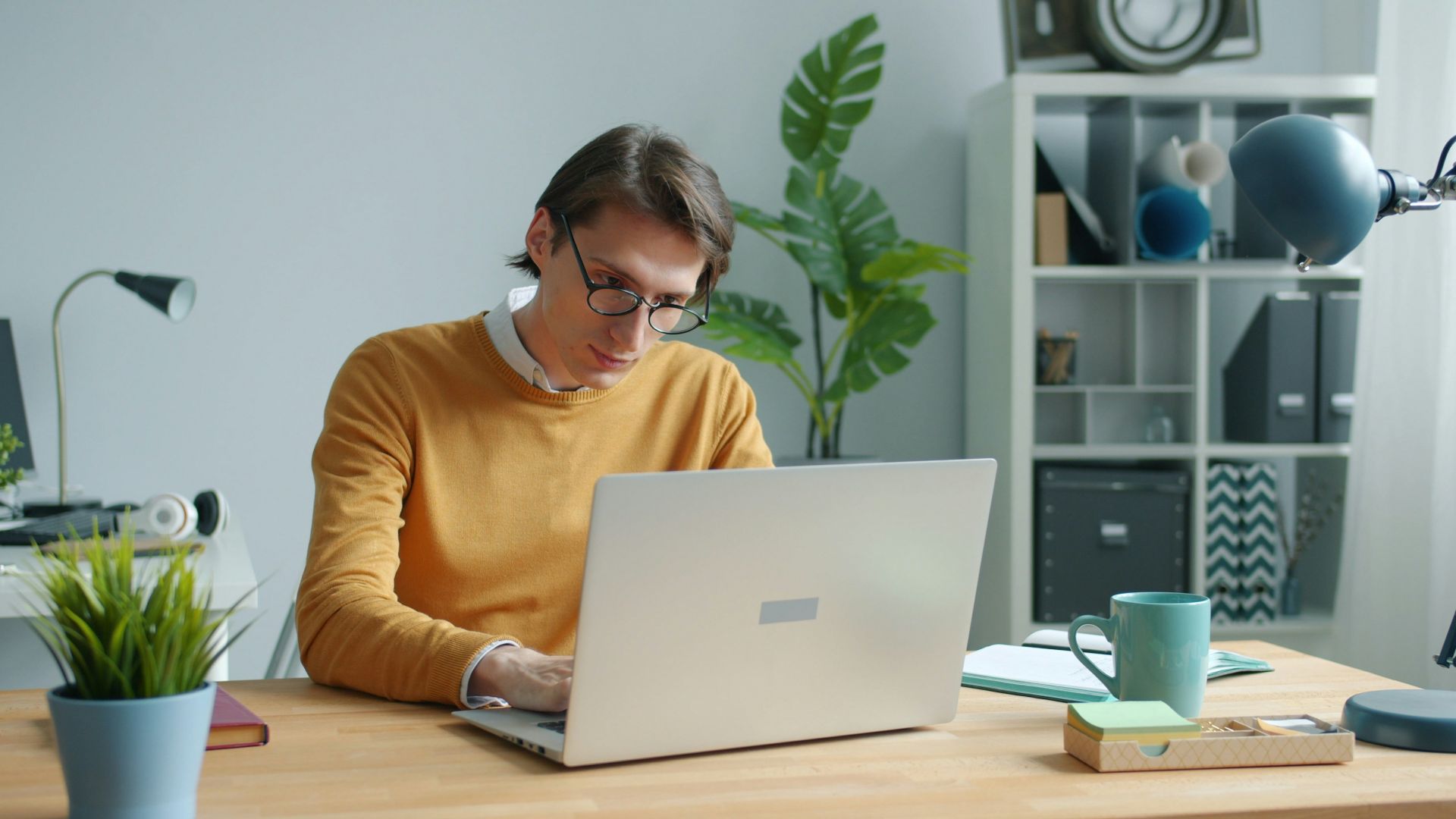 Man in yellow sweater working on laptop at desk.