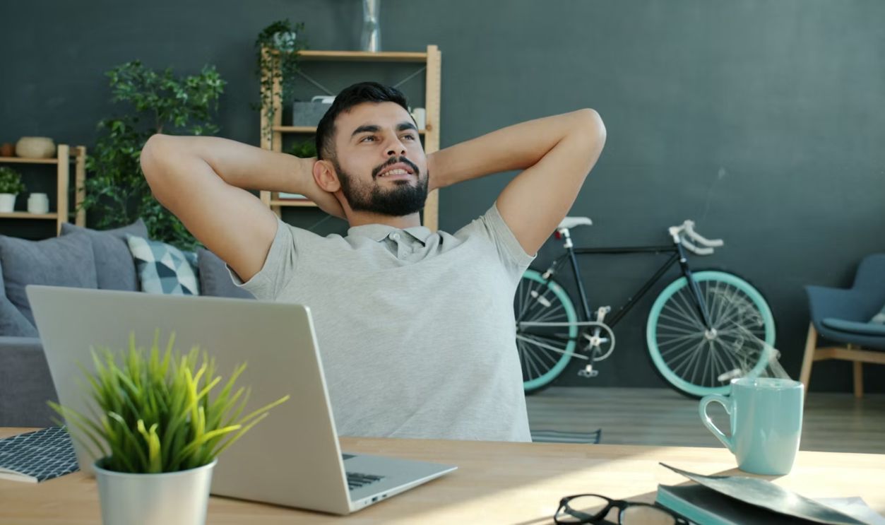 Man relaxing at desk with laptop and bicycle.