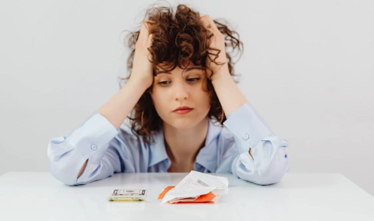 A Tired Woman in Blue Long Sleeves Looking at the Paper Money on the Table