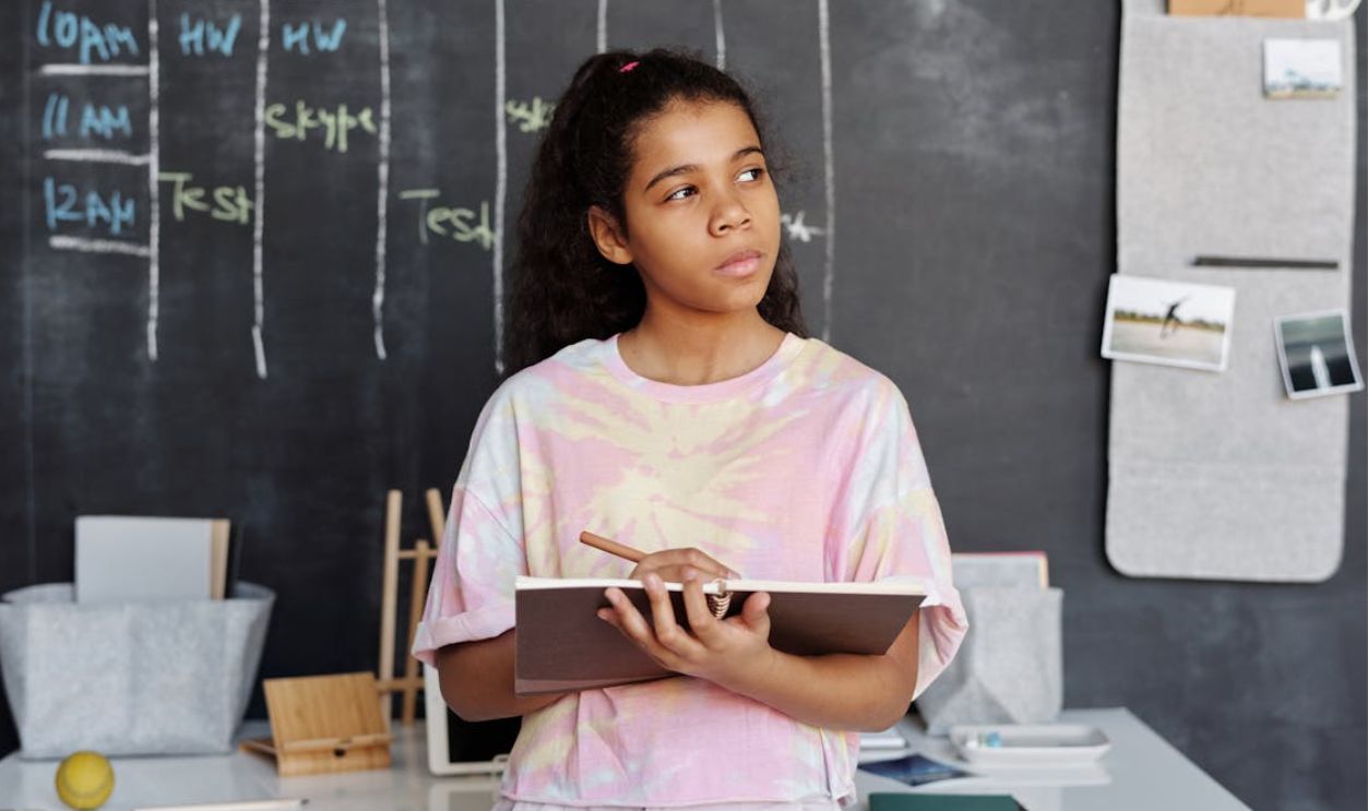 Woman in Pink and Yellow Crew Neck T-shirt Holding Brown Notebook