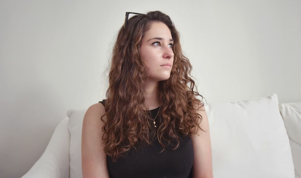 woman looking off to the right on a couch alone, daydreaming
