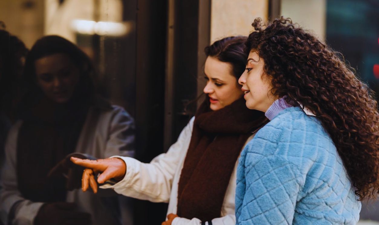 Content young multiethnic women choosing clothes standing on street near boutique showcase