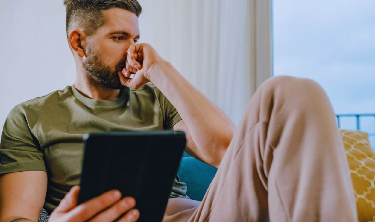 Man Sitting on Sofa Holding a Computer Tablet