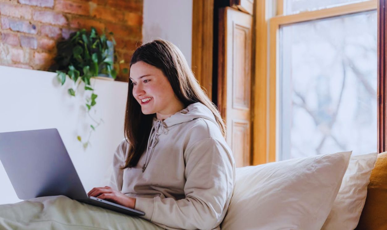 Positive woman browsing laptop in bedroom during remote work