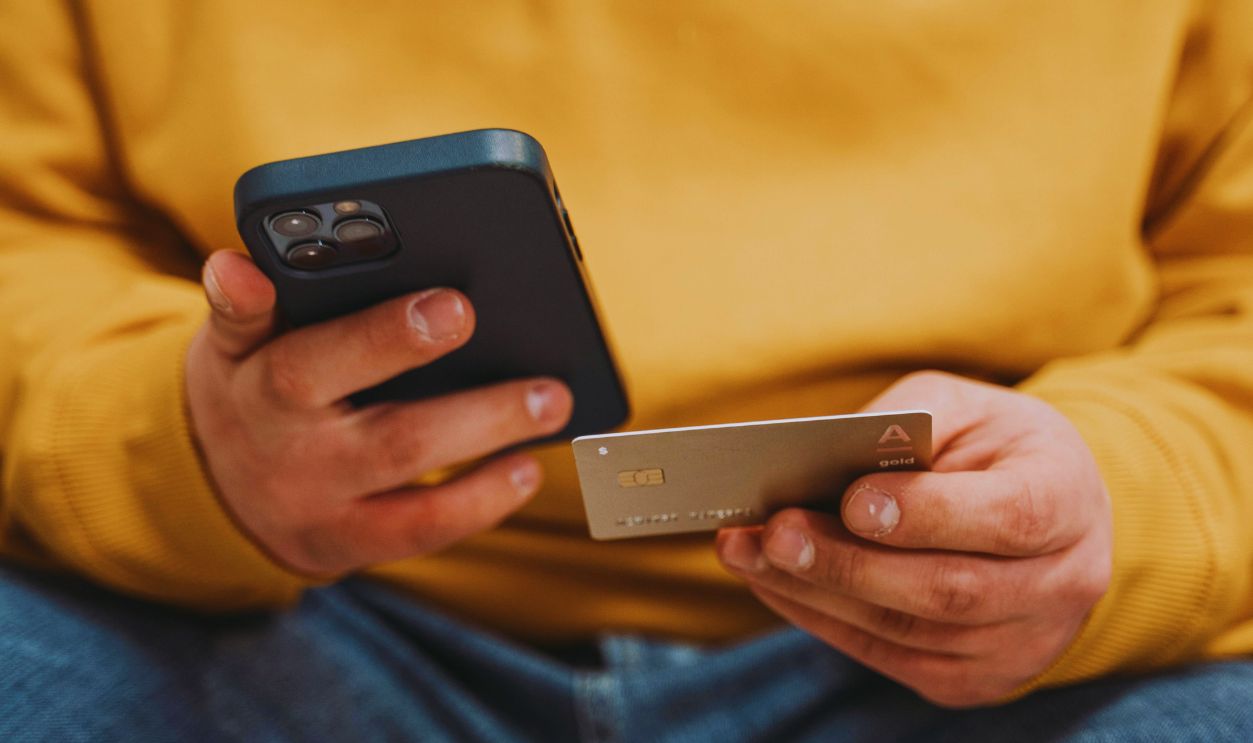 Man Wearing Yellow Jacket Holding a Smartphone and Credit Card