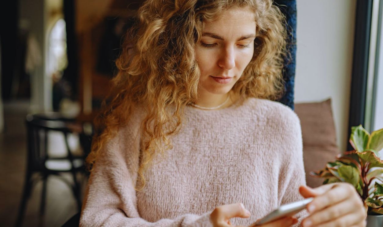 A Woman Using an Iphone Wearing a Sweater