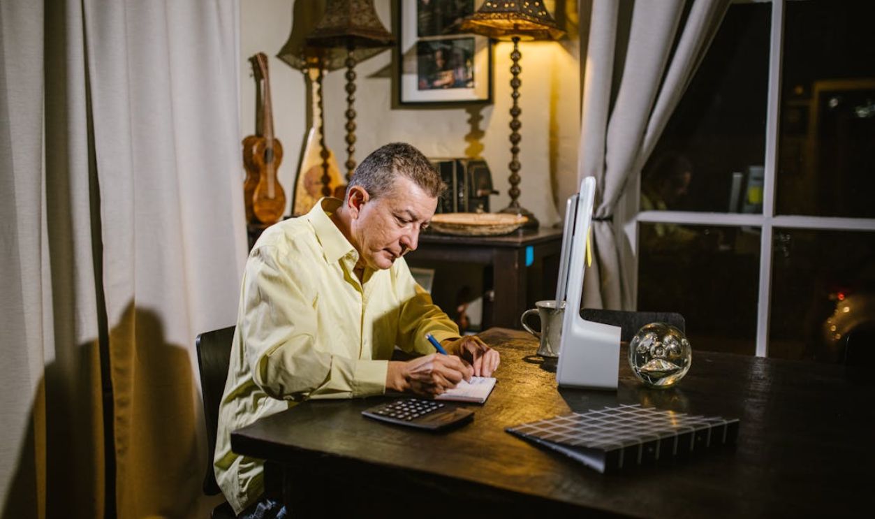 An Elderly Man Sitting while Writing on Notebook