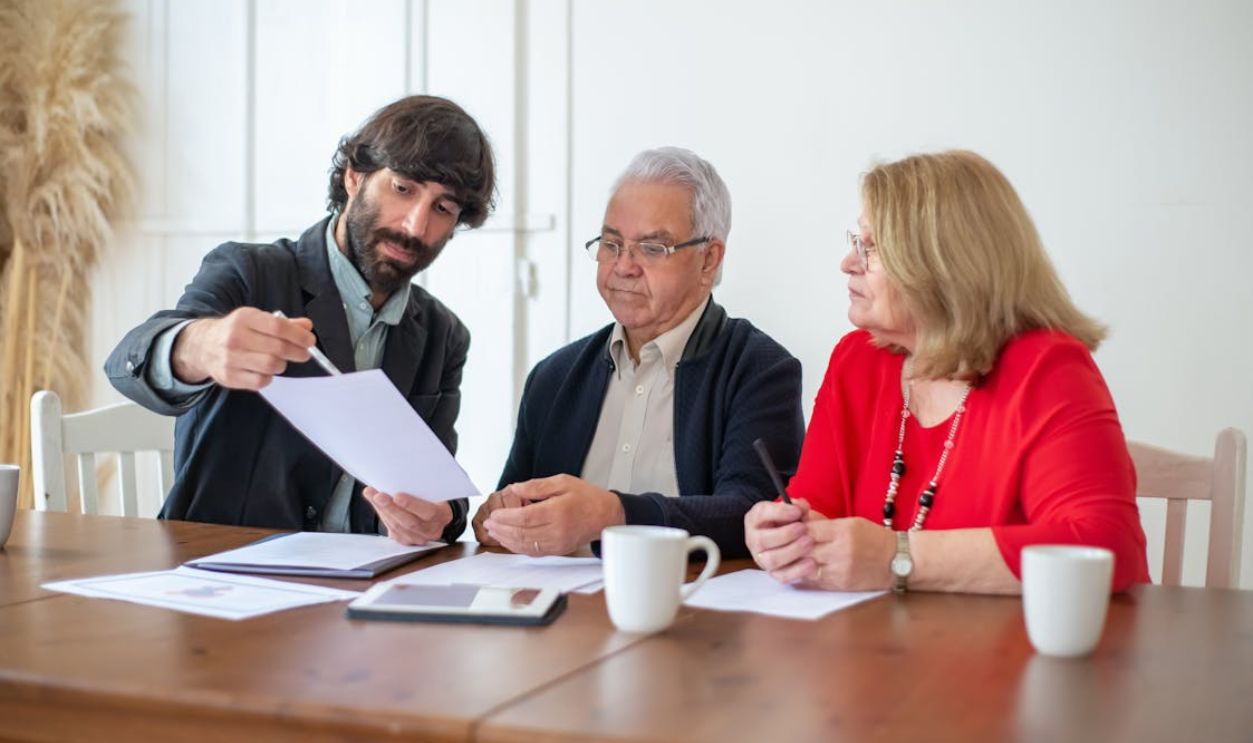 Bearded Man Showing Papers to a Couple Sitting at the Table