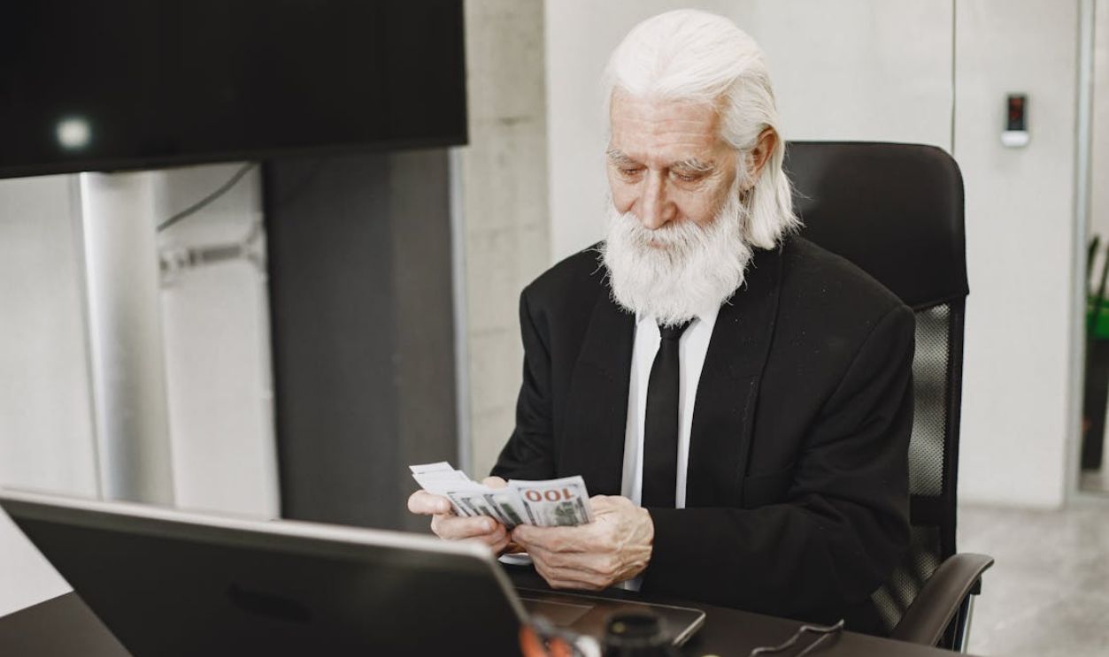 Elderly Man Counting Money in Office