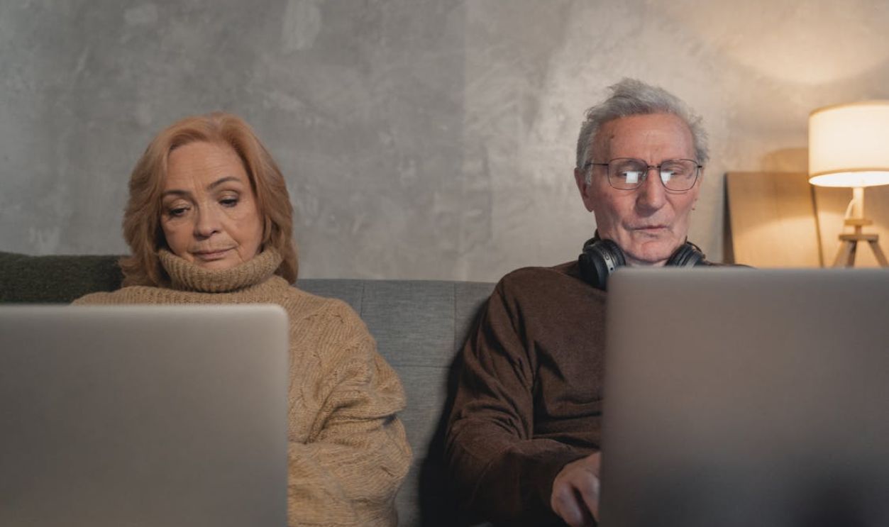 Elderly Man And Woman Sitting On Couch Using Laptop Computers