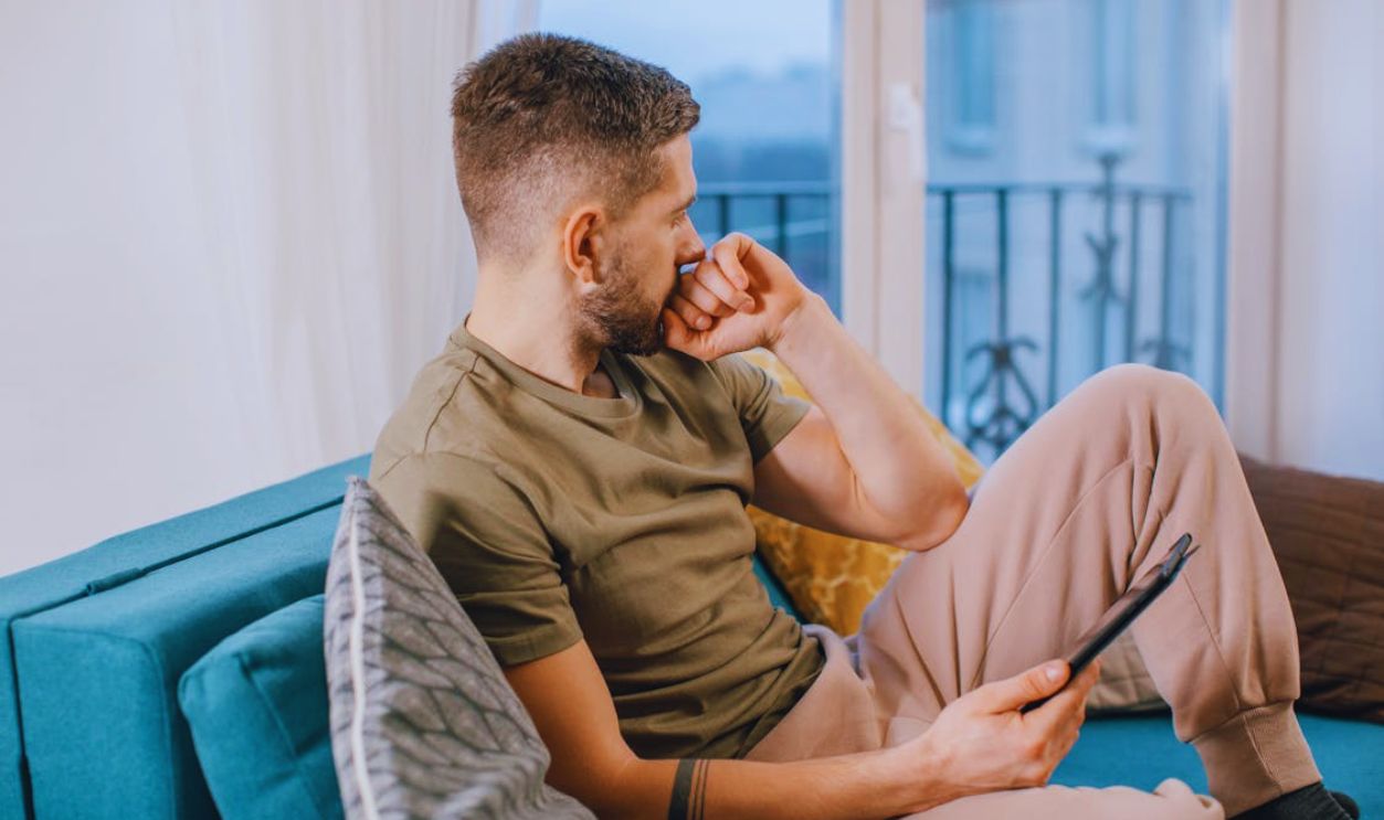 Man Sitting on Blue Couch Holding a Computer Tablet
