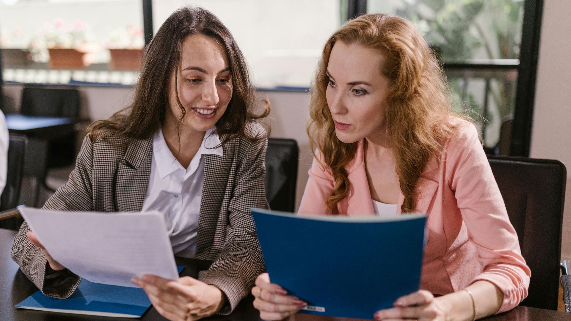 Two businesswomen reviewing documents together in an office setting, emphasizing teamwork and cooperation.