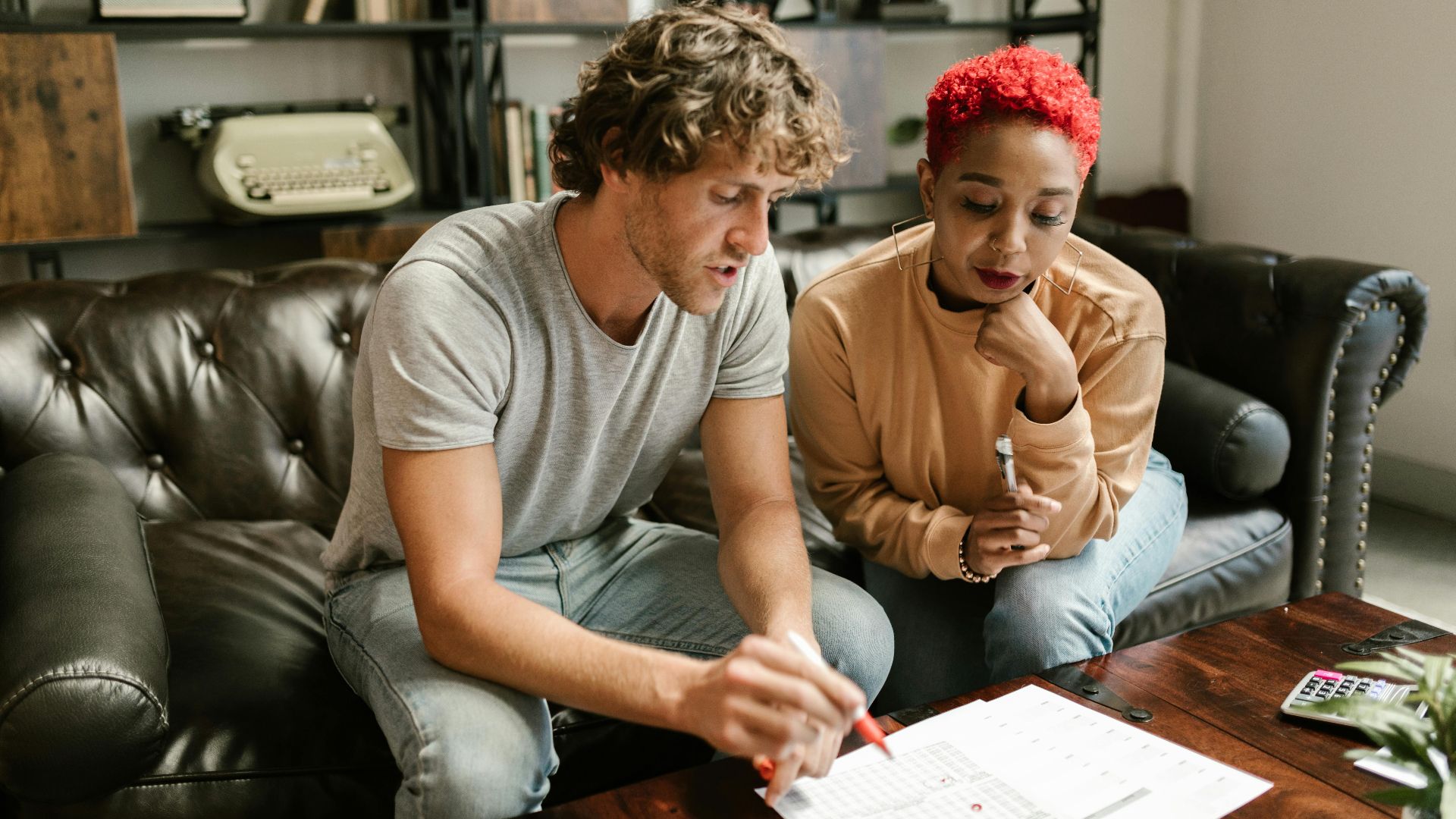 A couple sitting on a sofa examines documents in a cozy, modern living room setting.