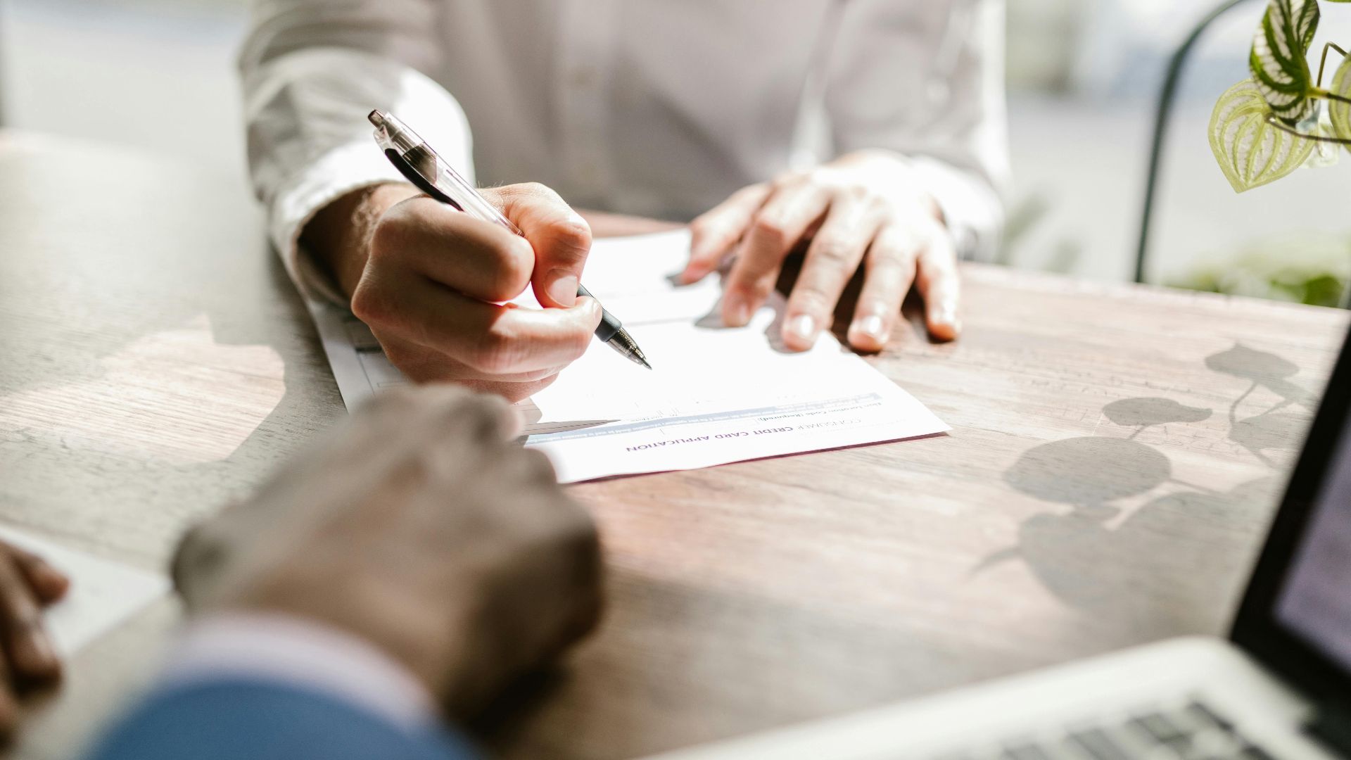 Close-up of people signing a document at a desk, highlighting professional business interaction.