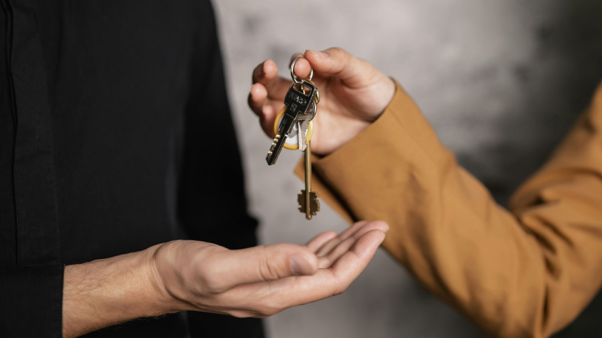 Detailed close-up of one person handing over keys to another, symbolizing a real estate transaction.