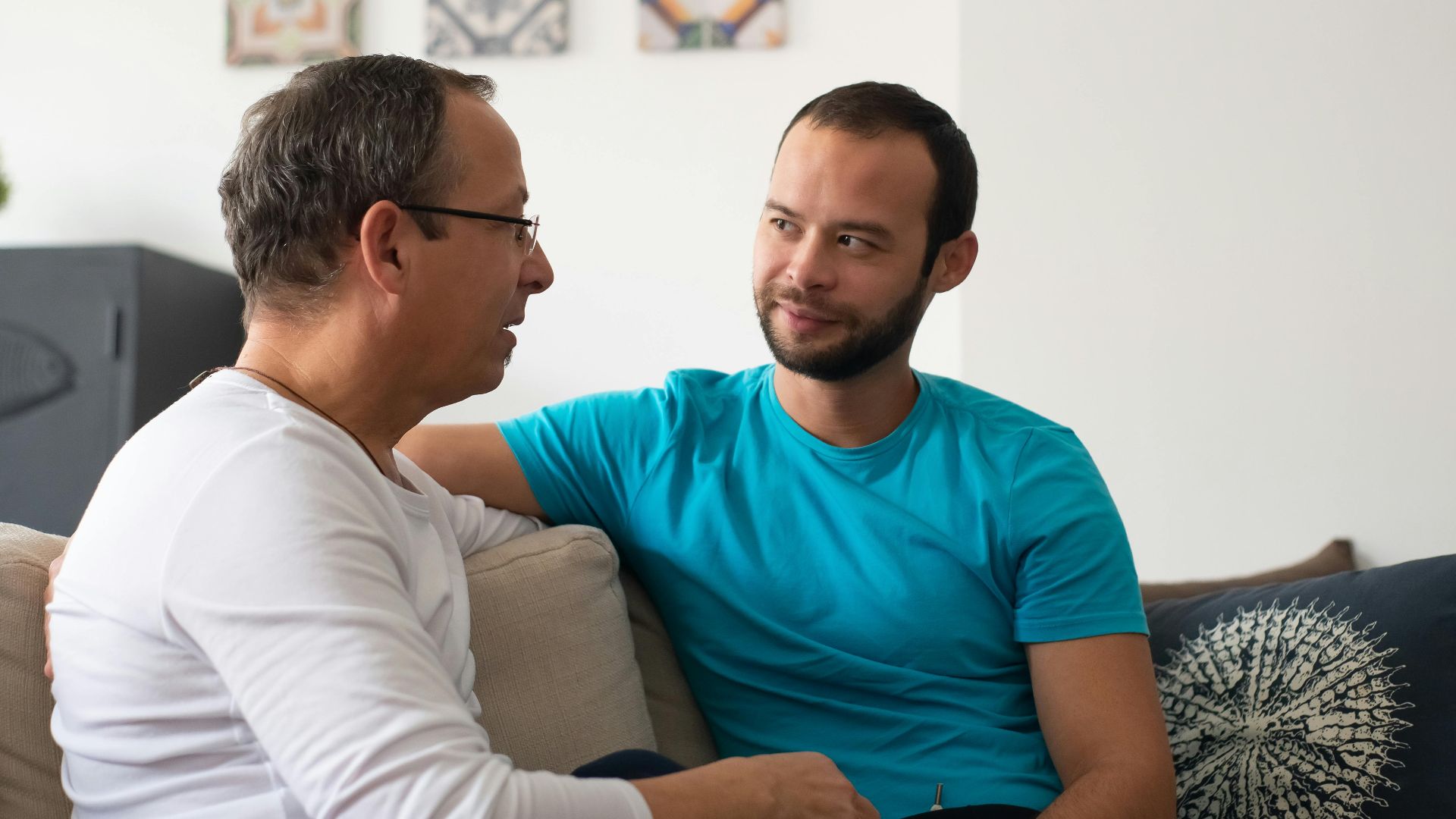 Two men share a heartfelt conversation on a cozy sofa in a modern living room.