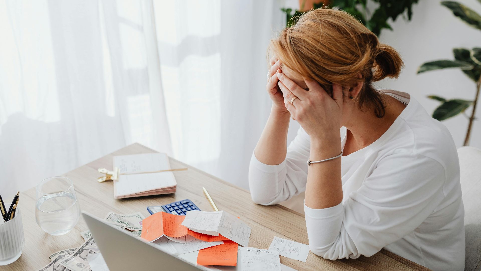 Woman stressed over financial receipts at a desk, dealing with expenses and calculations.