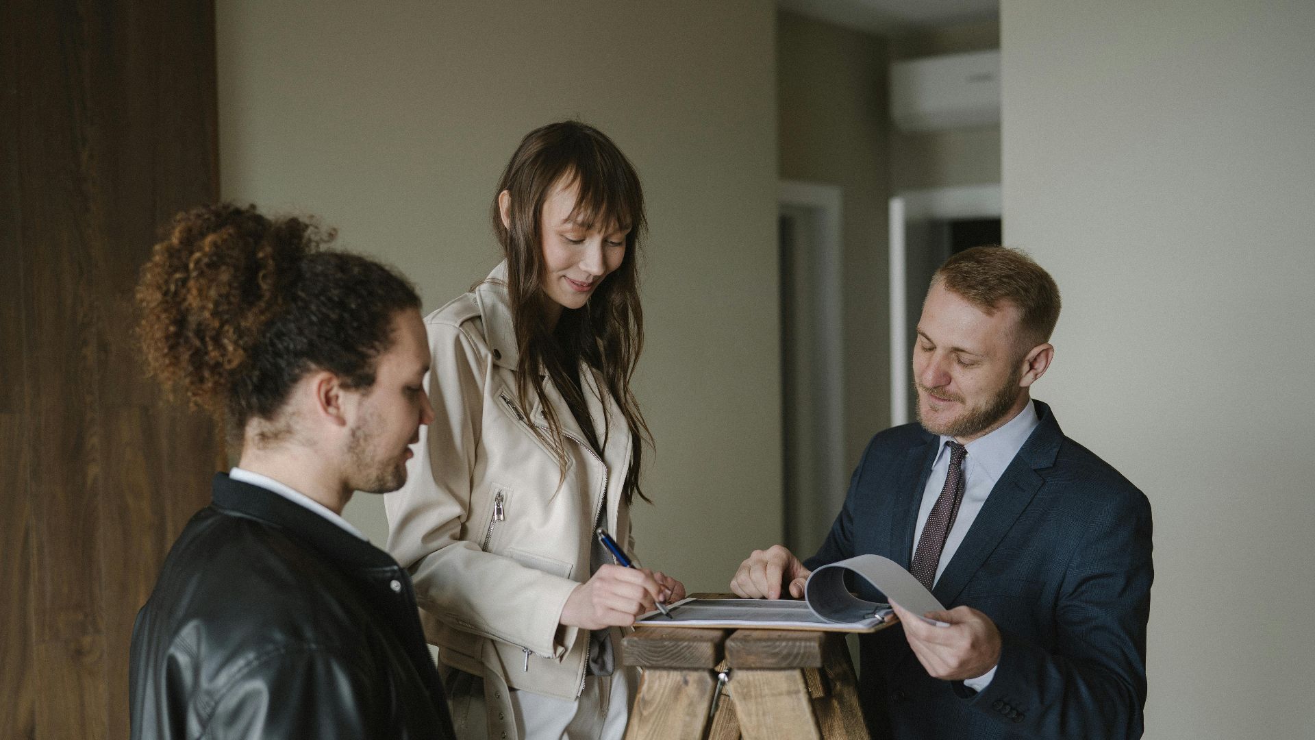 A couple signing real estate documents with a realtor inside a new apartment.