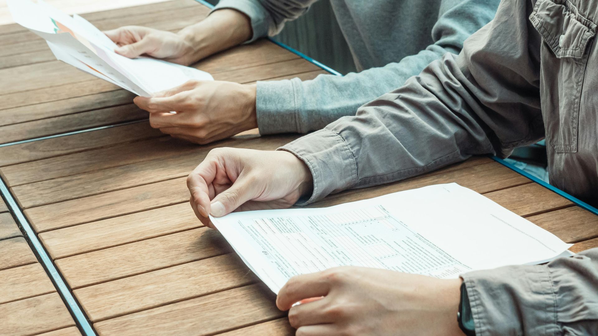 Two people reviewing business documents at an outdoor table, focused on paperwork.