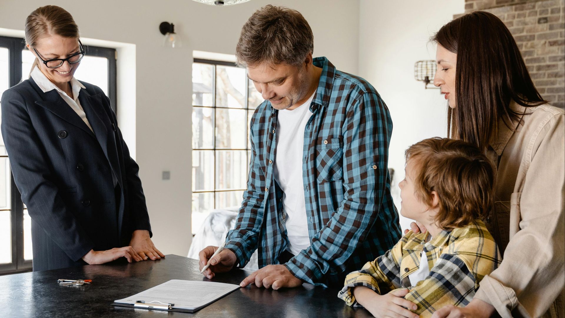 Family with a child signing a real estate agreement in a bright, modern kitchen with a realtor.