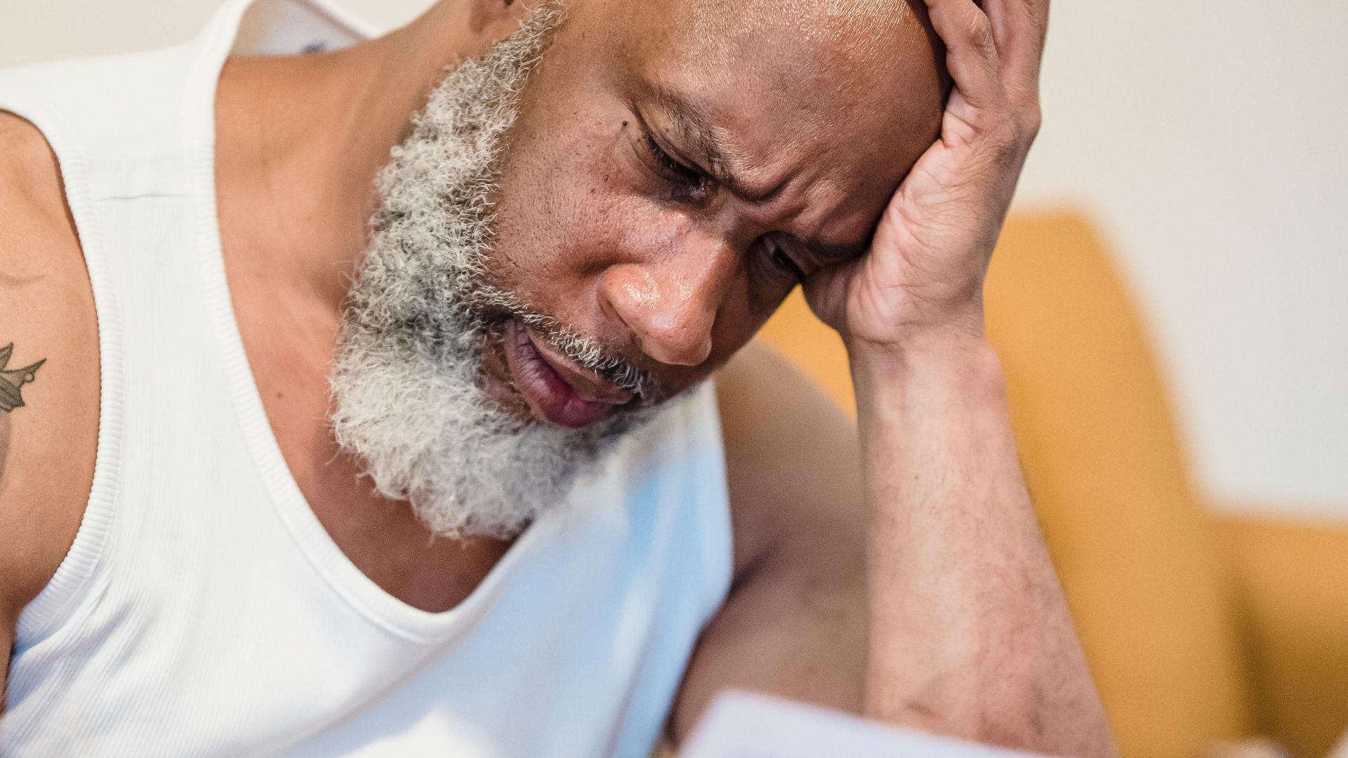 Middle-aged man in distress reading paperwork on a couch at home.