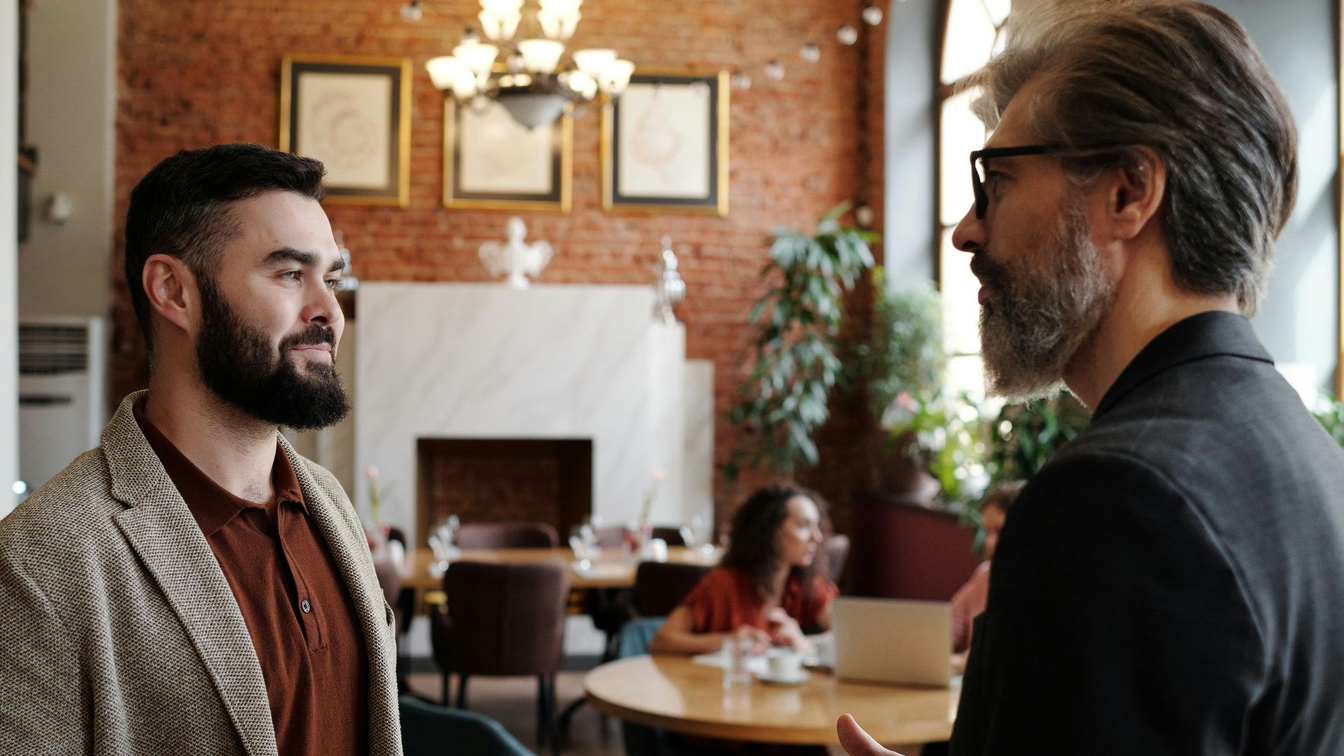Two men engaged in a conversation inside a stylish cafe with brick walls and elegant decor.