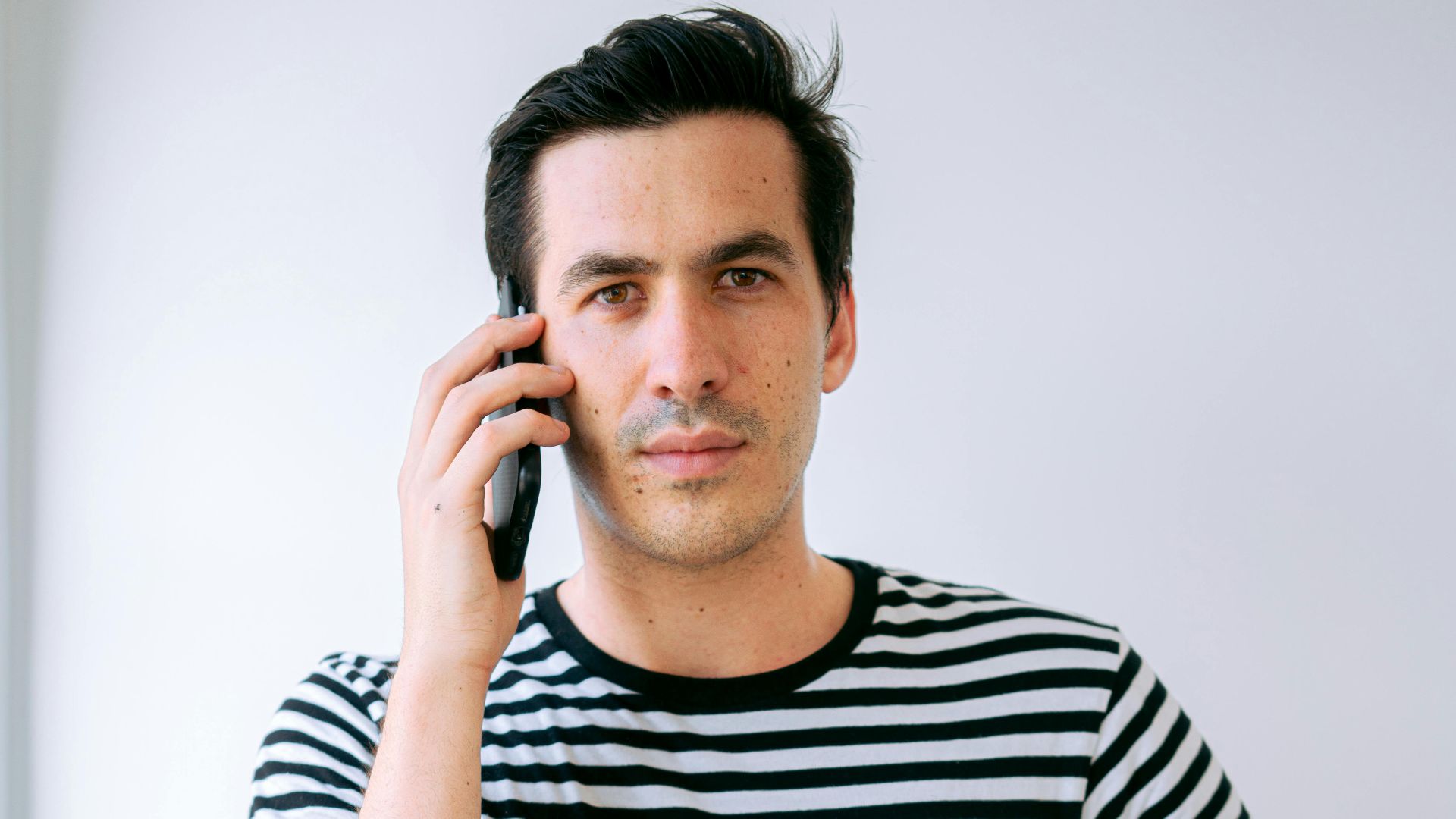 Portrait of a man in a striped shirt talking on his phone indoors.