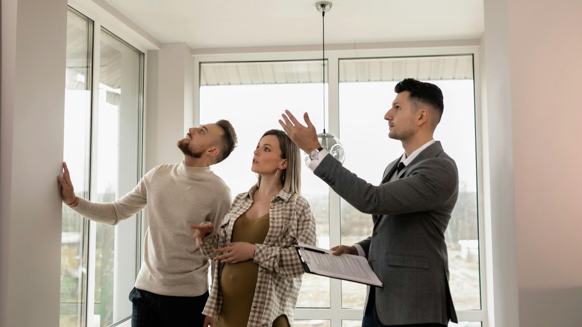 A young couple inspects a modern apartment with a real estate agent during a daytime viewing.