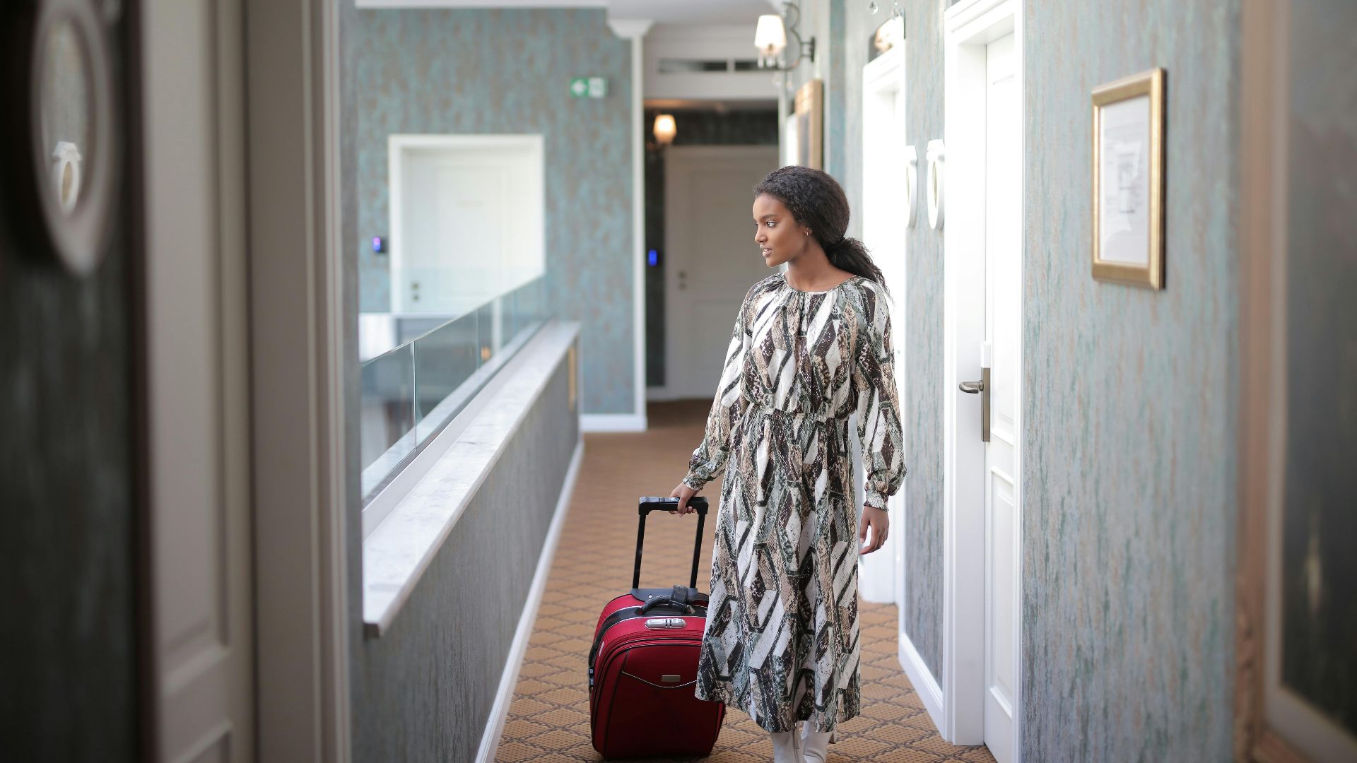A woman walks with luggage through a stylish hotel corridor, embodying travel elegance.