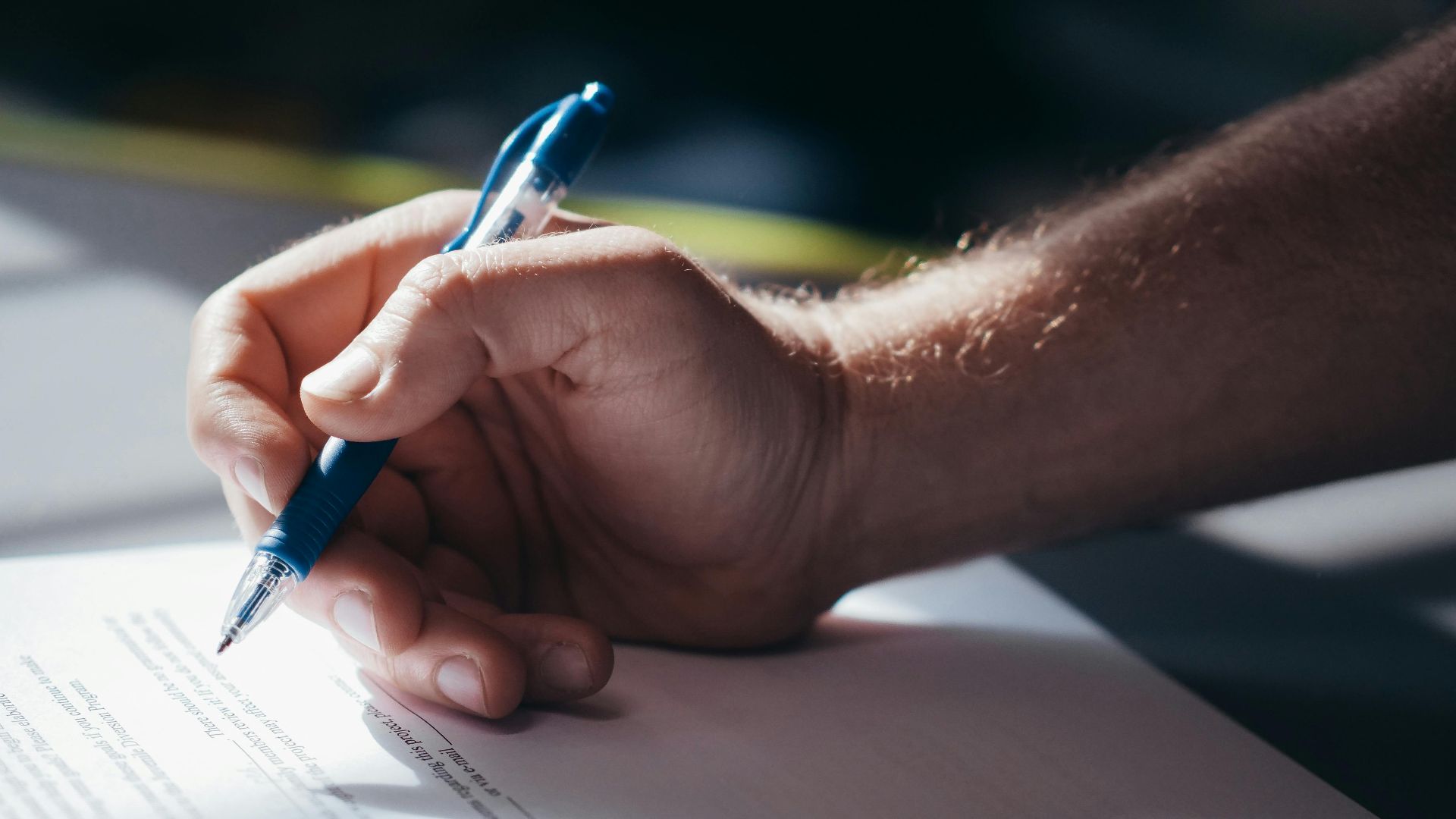 Detailed shot of a hand holding a blue pen while signing a document. Ideal for legal and business themes.