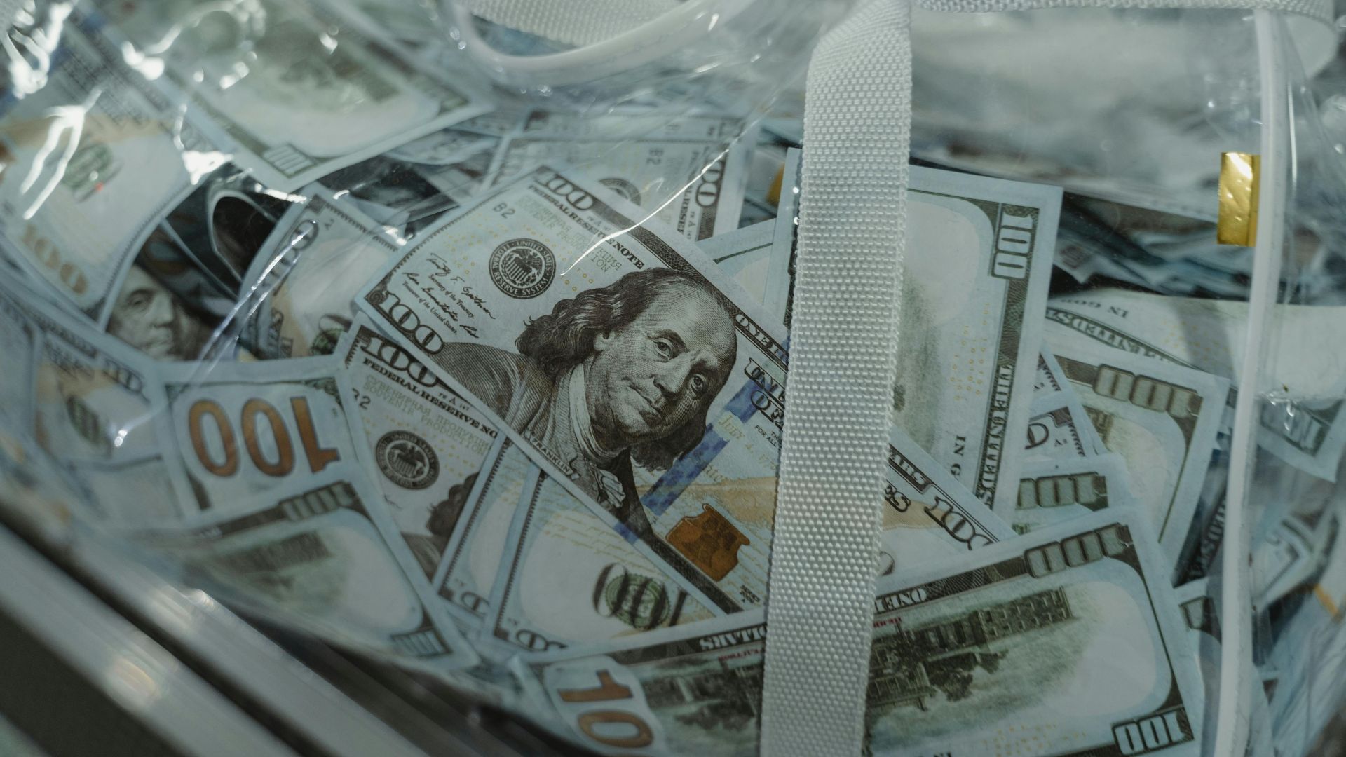 Close-up of transparent bag containing hundred dollar bills, symbolizing wealth.