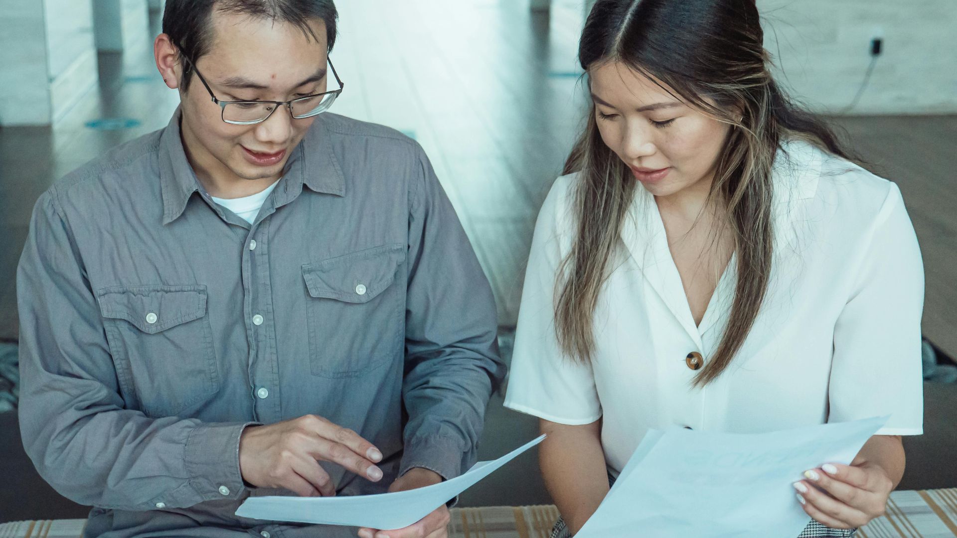 Two coworkers reviewing documents in a modern office, focused on teamwork and planning.
