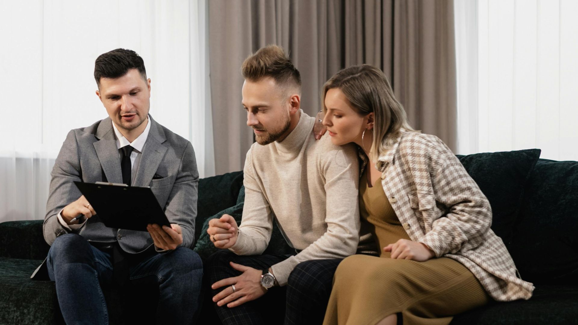 A real estate agent shows a property listing to a couple in a modern living room.