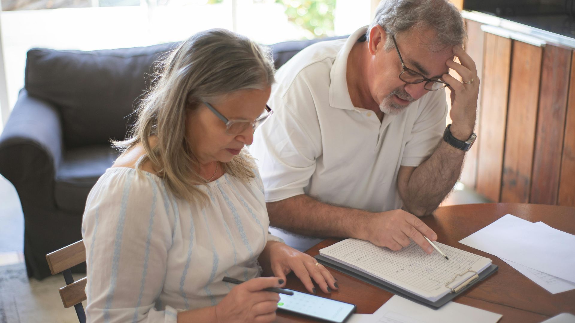 Elderly couple reviewing bills and documents at home, focusing on finances and technology.