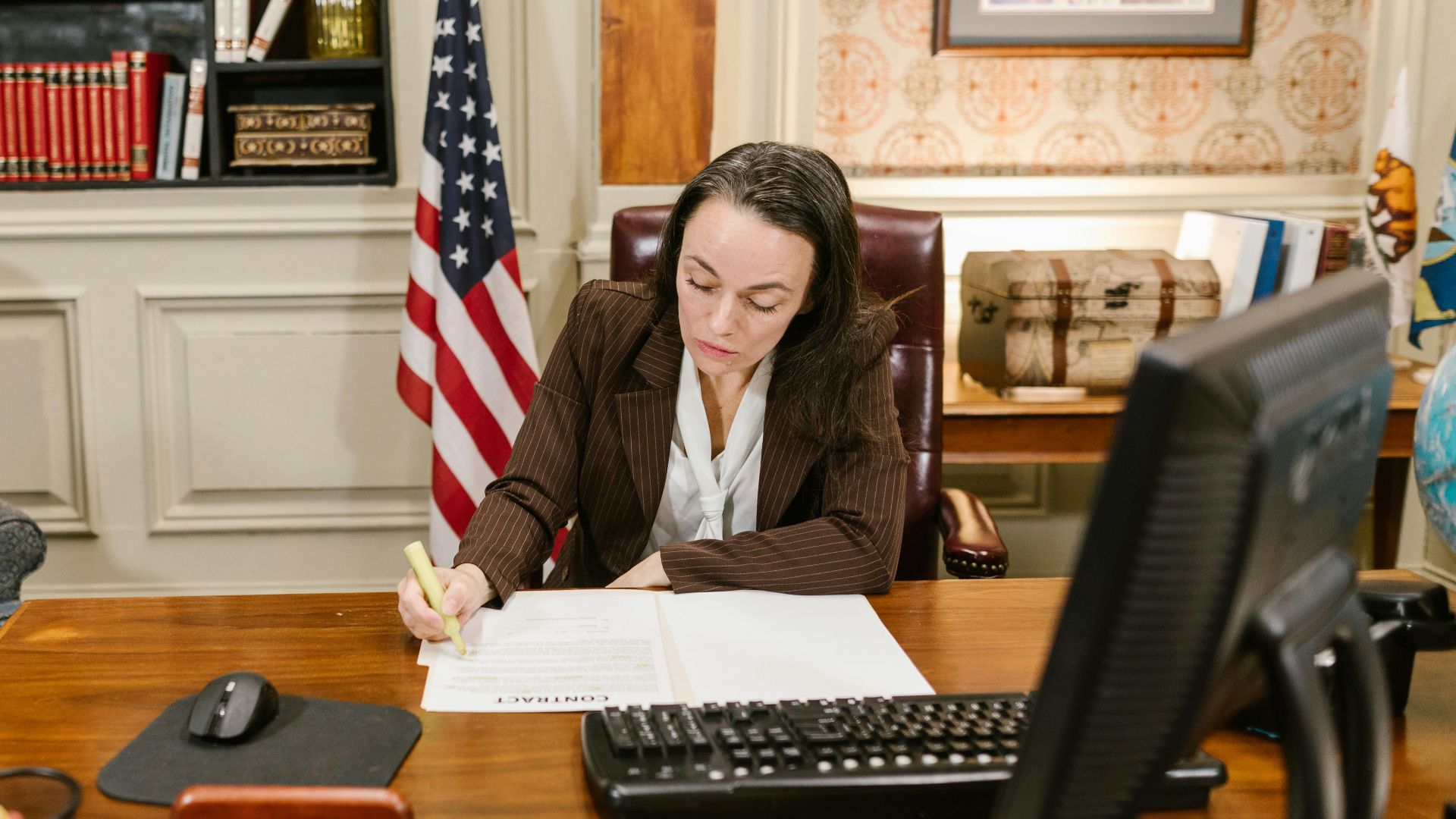 Female attorney in a law office signing legal documents at her desk, surrounded by legal books and symbols of justice.